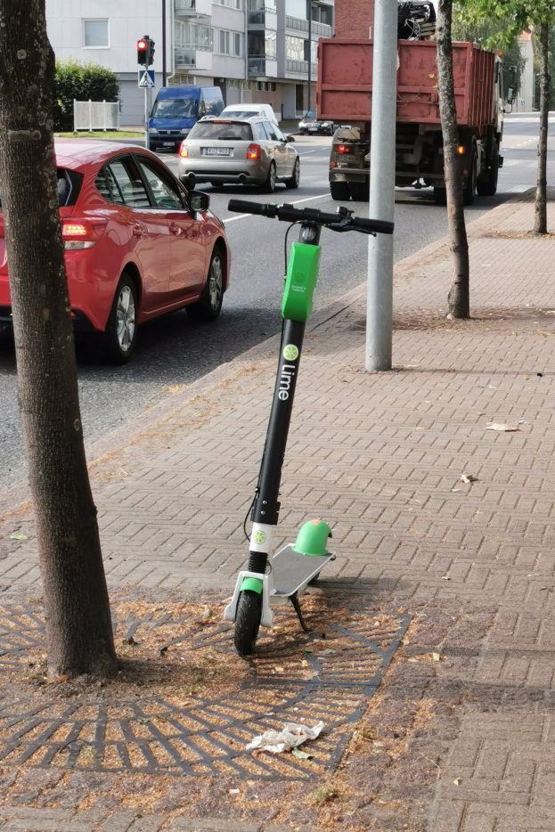 Elektroroller auf einer Straße neben einem Baum geparkt mit Fahrzeugen und Gebäuden im Hintergrund.