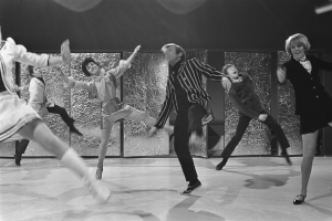 Eine Gruppe von Menschen, die auf einer Bühne vor einer Wand tanzen, in Schwarz-Weiß aufgenommen und alle tragen Schuhe.