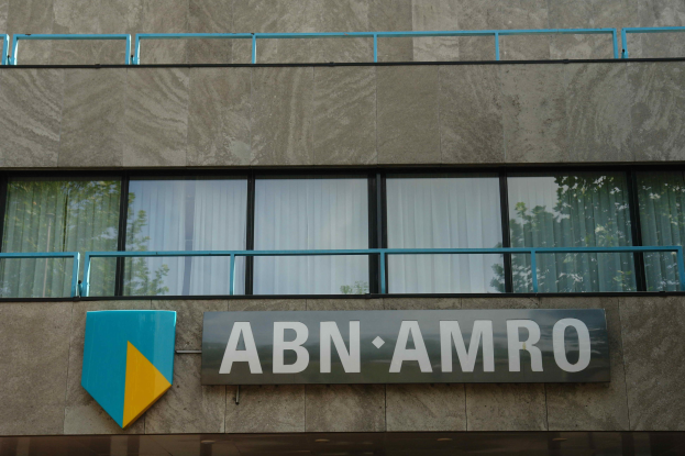 Ein modernes Bürogebäude mit "ABN AMRO"-Schriftzug, einer Tafel, die seinen Status als Hauptsitz anzeigt, Geländern und Vorhangfenstern, die auf eine EU-Strafe von 1,5 Milliarden Dollar hinweisen.