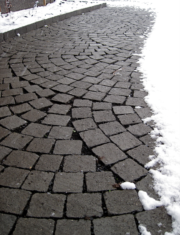 Ein Kopfsteinpflasterstraße mit einer leichten Schneeschicht, ein Zaun im Hintergrund, der eine friedliche Winterszene schafft.