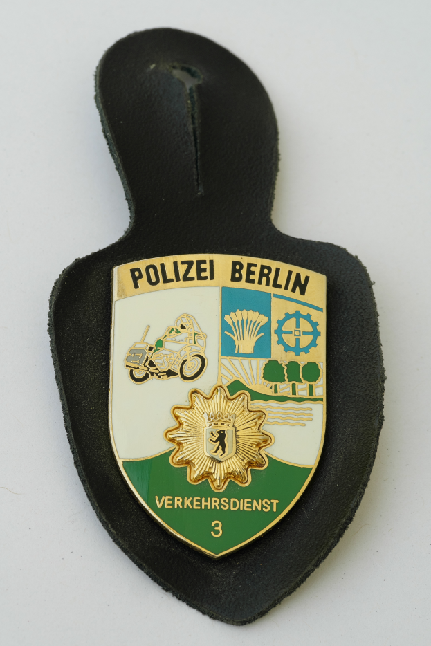 Ein Polizeistern mit der Aufschrift "Polizei Berlin" in fetter schwarzer Schrift auf einem blauen Schild mit einem weißen Stern und einem weißen Rand.