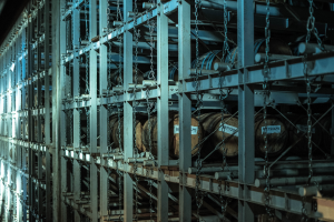 Ein großes Lagerhaus mit zahlreichen Fässern, die mit Metallstangen und Ketten verbunden sind und in einem organisierten Regalsystem gestapelt sind.