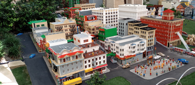 Ein detailliertes Lego-Modell einer Stadt mit Gebäuden, Bäumen, Fahrzeugen, Menschen, Straßen und Gras.