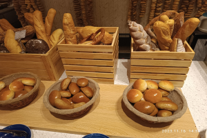 Holztisch mit Körben voller Brot, Tellern und Löffeln in einer Pariser Bäckerei mit einer wasserzeichenverzierten Wand im Hintergrund.