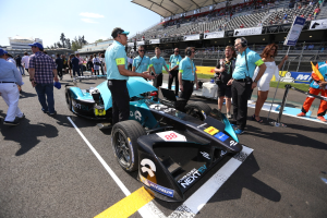 Eine Gruppe von Menschen feiert um ein Formel-E-Rennwagen auf der Strecke, mit einem Stadion voller Zuschauer im Hintergrund an einem klaren blauen Himmel.