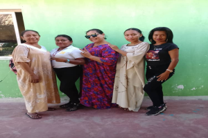 Eine Gruppe von Frauen steht vor einer grünen Wand mit einem Fenster auf der linken Seite und nimmt an einer Internationalen Frauentags-Veranstaltung teil.