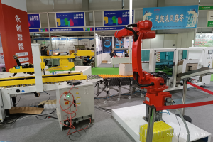 Gruppe von Robotern auf einem Tisch in einer Fabrikumgebung mit Maschinen, Kabeln, Leiterplatten und Menschen im Hintergrund.