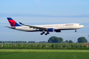 Ein Boeing 787-9 Dreamliner der Delta Air Lines startet vom Frankfurter Flughafen mit grünem Gras darunter, Laternenpfählen und Bäumen im Hintergrund, einem Turm auf der rechten Seite und weißen Wolken am Himmel.