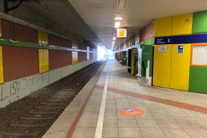 Ein Bahnhof in Berlin, Deutschland, mit einem Zug auf den Schienen, beleuchteter Deckenbeleuchtung, Graffiti an der linken Wand und einigen Gegenständen auf der rechten Seite.