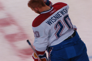 Ein Eishockeyspieler in einem "Wisniewski"-Trikot steht auf dem Eis und hält einen Eishockeyschläger, mit konzentrierter und entschlossener Miene.