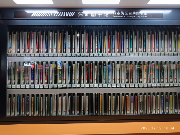 Eine gut beleuchtete Bibliothek mit hohen Bücherregalen voller Bücher, ein Textbrett und ein Wasserzeichen unten, das einer Selbstbedienungsbibliothek der Stadtblocks ähnelt.