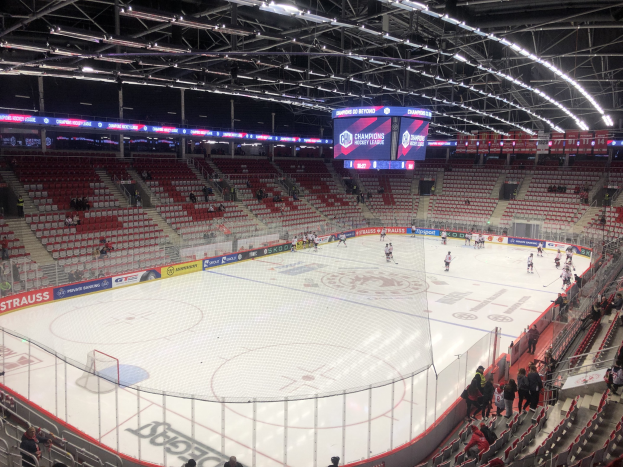 Eishockey-Spiel in einer großen Arena zwischen den St. Louis Blues und den Detroit Red Wings, mit Zuschauern auf den Sitzen und Stehplätzen in der Nähe der Eisfläche umgeben von einem Zaun und einem Bildschirm.