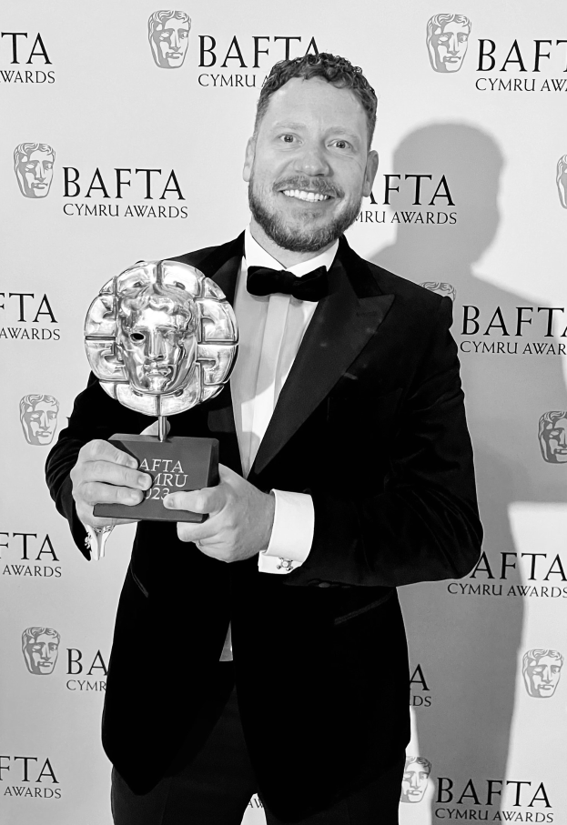 Ein Mann in einem Smoking, der eine BAFTA-Trophäe hält und vor einer Tafel mit "BAFTA Awards 2018" steht.