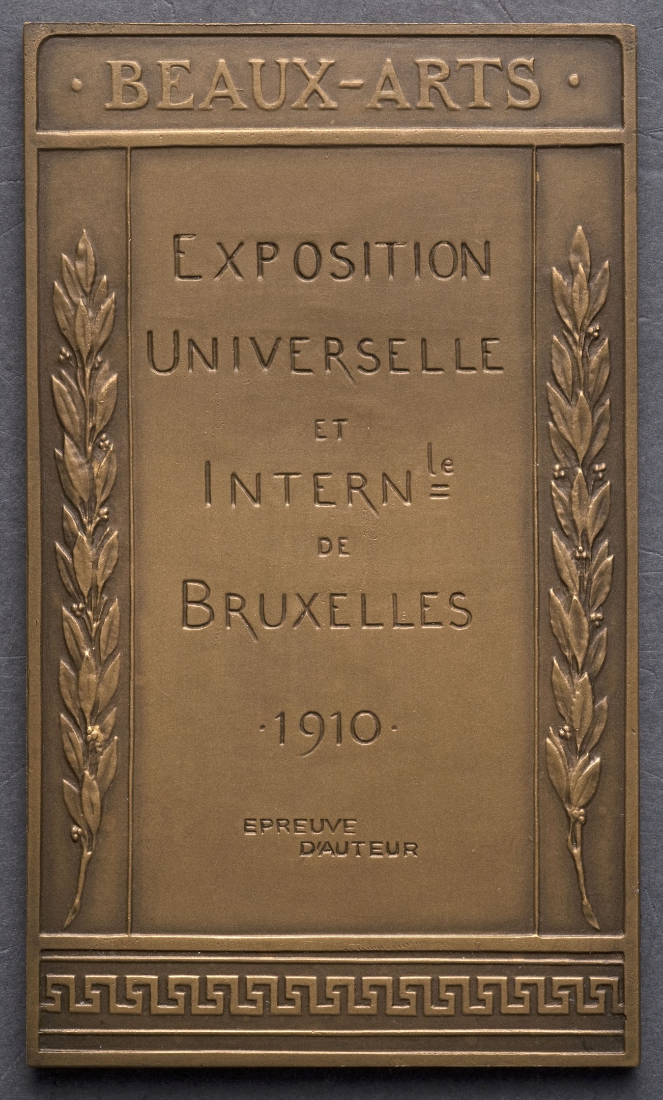 Bronzetafel mit der Inschrift "Exposition Universelle et Internationale de Bruxelles 1910" in fetter Schrift, umgeben von einem dekorativen Rahmen, mit einem Glanzfinish.