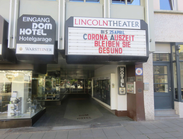 Außenansicht des Lincoln Theaters in Berlin, Deutschland, mit Glasfenstern und -türen sowie einer Tafel und einem durch die Fenster sichtbaren Innenraum mit einer belebten Stadtkulisse.