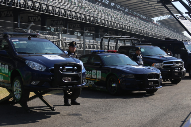 Polizeiautos vor einer Rennstrecke geparkt, Stadion mit Geländern und Maschendrahtzaun im Hintergrund.