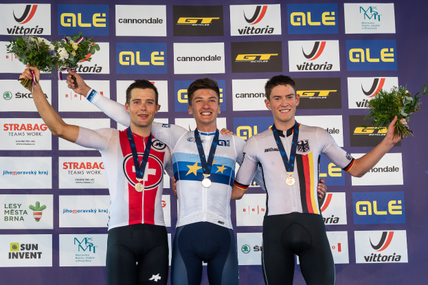 Drei Männer stehen auf einem Podium, jeder trägt eine Medaille und hält einen Blumenstrauß, im Hintergrund ist ein "Giro d'Italia"-Schild zu sehen.