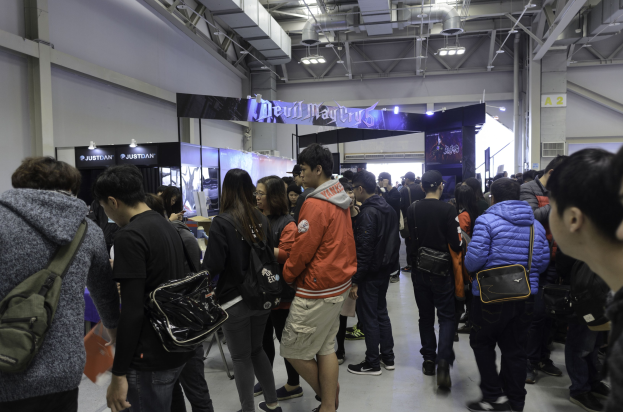 Eine Gruppe von Menschen vor einem Publikum an einer Gaming-Messe, mit Schildern, Lichtern und Rohren im Hintergrund.