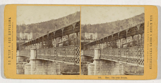 Schwarz-weiß-Fotografie einer Brücke, die einen Fluss in Leipzig, Deutschland, überspannt, mit Gebäuden, Bäumen und einem Hügel im Hintergrund.