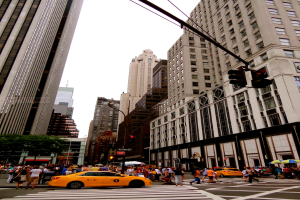 Eine Straßenszene in der Stadt mit Gebäuden, Ampeln, Fenstern, wenigen Passanten, Autos und Himmel.