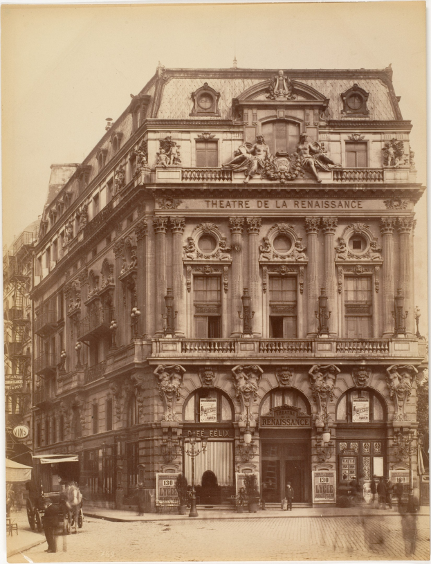 Schwarz-weiß-Foto des Théâtre de la Renaissance in Paris, das eine Fassade mit Fenstern, Säulen, Bögen und Skulpturen zeigt, mit ein paar Menschen und Fahrzeugen auf der Straße davor und dem Himmel im Hintergrund.
