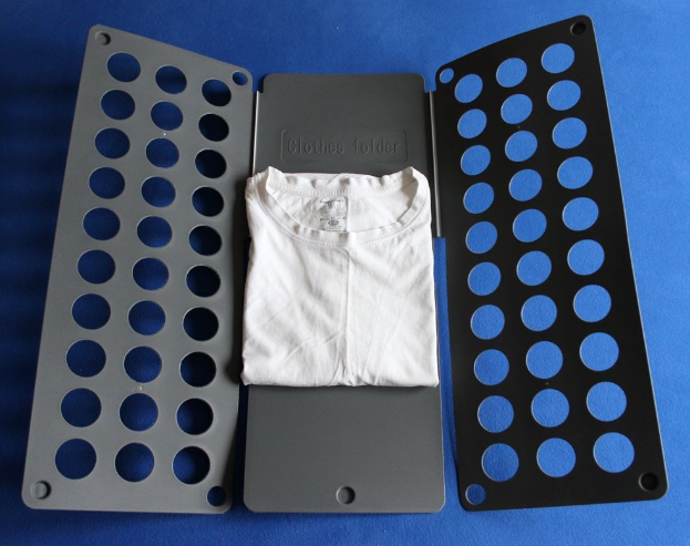 Ein weißes T-Shirt auf einer blauen Oberfläche neben einem schwarzen und aschfarbenen Kleiderordner mit mehreren Löchern.