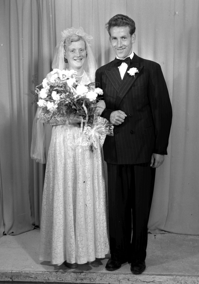 Ein Mann und eine Frau stehen nebeneinander auf einer Bühne, lächeln und die Frau hält einen Blumenstrauß in der Hand.