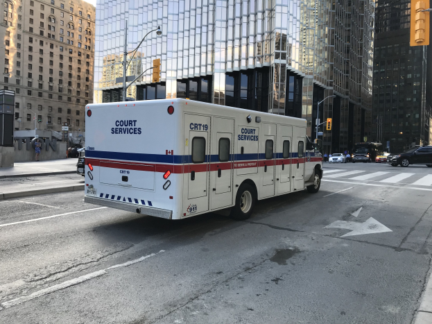 Ambulanz auf einer Stadtstra├če mit hohen Geb├Ąuden, Stra├čeninfrastruktur und Passanten bei Tageslicht.