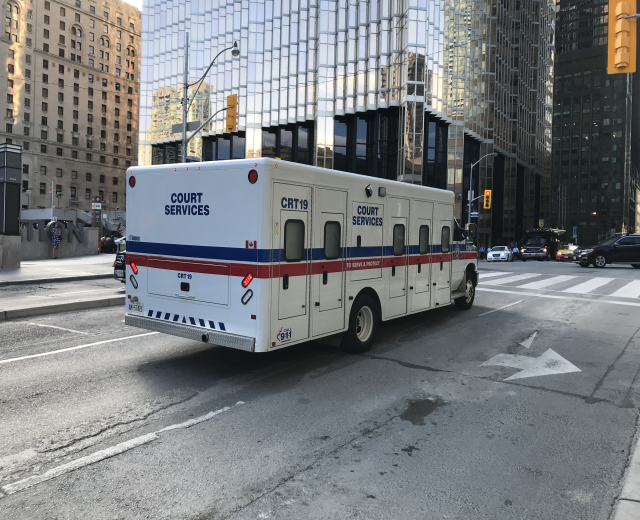 Ambulanz auf einer Stadtstra├če mit hohen Geb├Ąuden, Stra├čeninfrastruktur und Passanten bei Tageslicht.