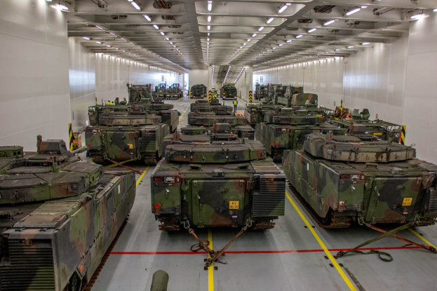 Ein grosser Militaraustellungsraum mit einer Decke voller Lampen, der eine ordentliche Reihe von Militarafahrzeugen entlang der Waende enthaelt.