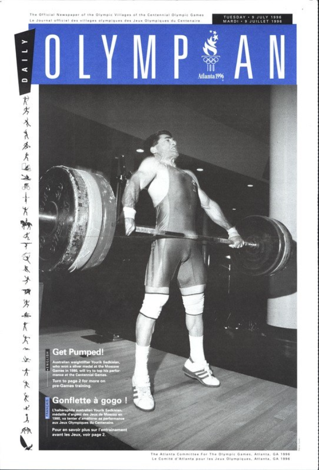 Schwarzes und weißes Foto eines Mannes in einem Krafttraining-Outfit, der eine Hantel stemmt, mit 'Olympian Magazine'-Text oben und entschlossener Miene.