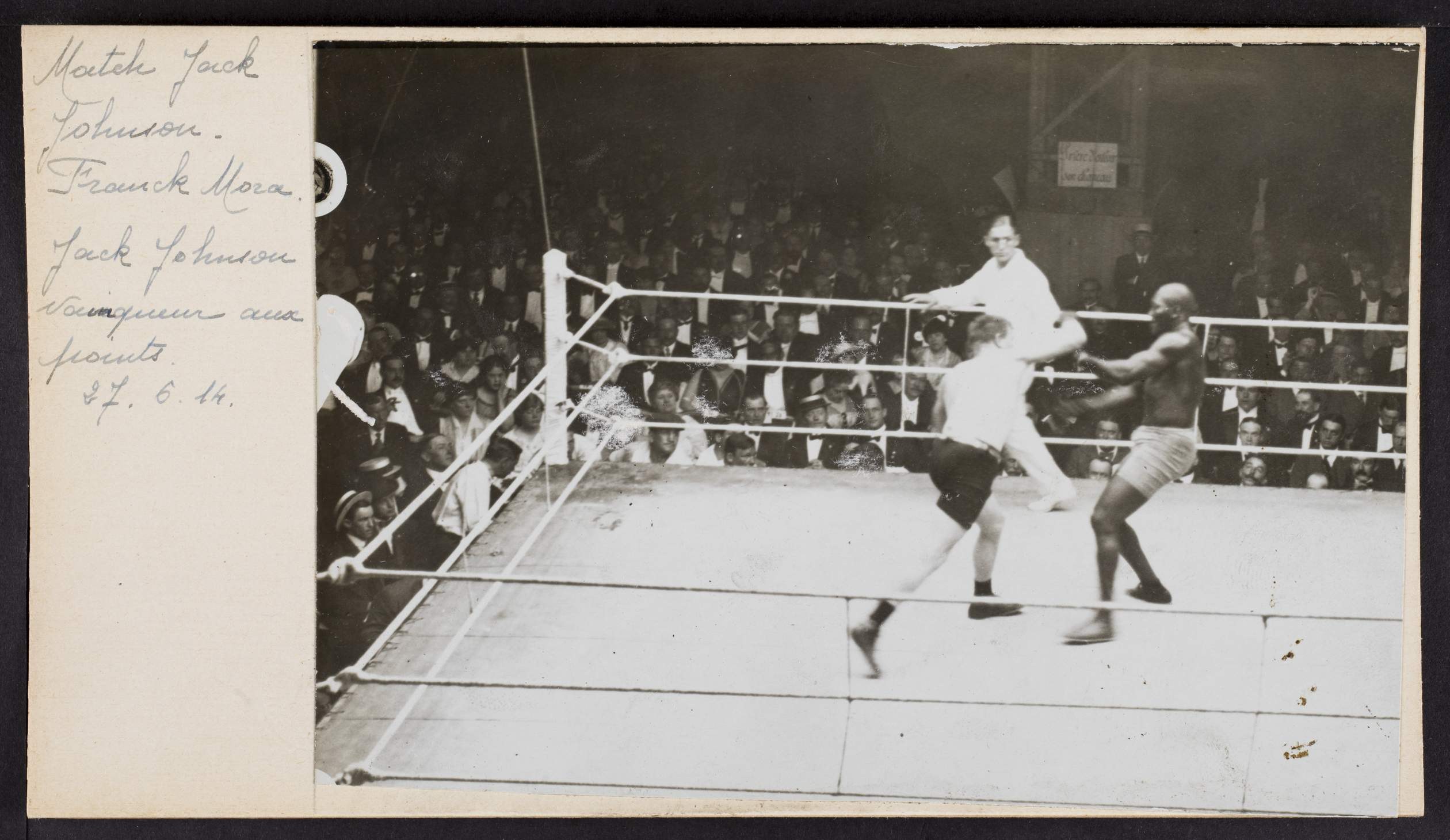 Schwarzes und weißes Foto von zwei Boxern in einem Ring, beschriftet mit 'Jack Johnson vs Frank Morgan', mit Zuschauern und einer Wand im Hintergrund.