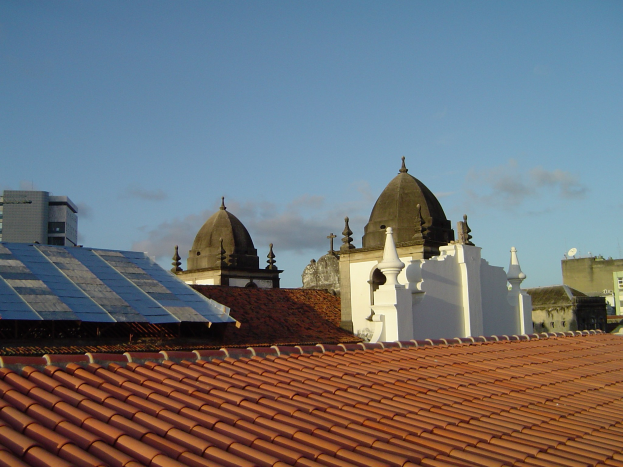 Eine Stadtansicht mit ein paar Gebäuden im Vordergrund und einem blauen Himmel im Hintergrund, die Solarpanels auf dem Dach eines Gebäudes zeigt.