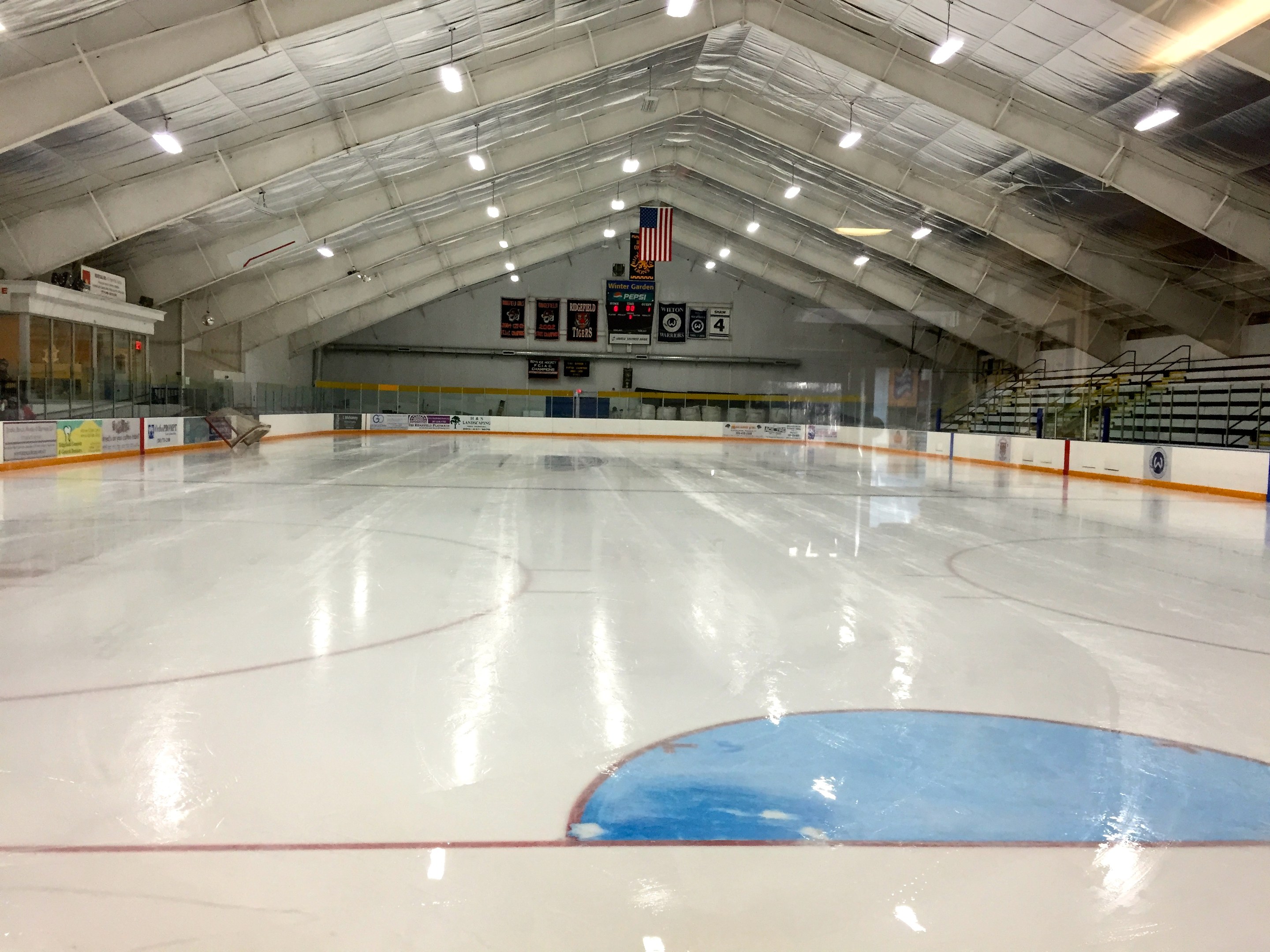 Großes Hallen-Eisstadion mit Deckenbeleuchtung, Werbetafeln, Treppen mit Geländern und einigen Menschen in einer Sportanlage.