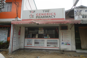 Ein Apotheken-Schild mit der Aufschrift "The Generics Pharmacy" vor einem Gebäude mit umliegenden städtischen Elementen und einem klaren Himmel.