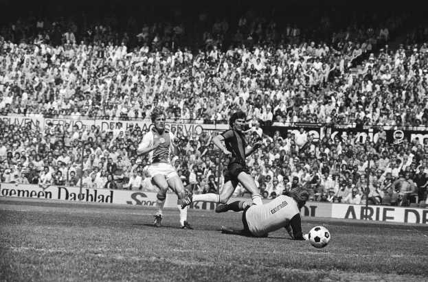 Schwarzes Foto von Männern, die Fussball auf einem Feld spielen, mit Zuschauern im Hintergrund und einer Bundesliga 1978-79 Ajax 1-1 Hannover 96 Fahne.