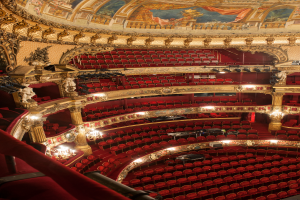 Ein Blick hinter die Kulissen des Opernhaus-Auditoriums in London mit Sitzreihen, Geländern, Säulen, Lampen und Wandskulpturen sowie einer Deckenmalerei.