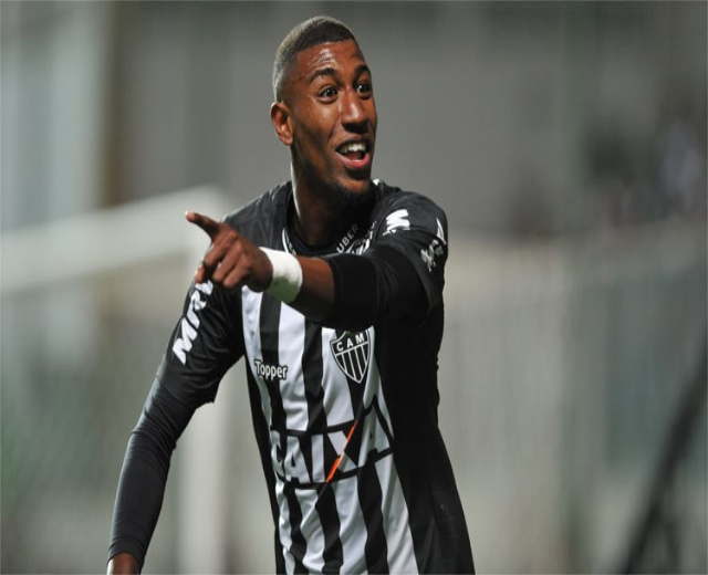 Fußballspieler in schwarzem und weißem gestreiftem Trikot, der grinsend ein Tor feiert, Hintergrund unscharf.