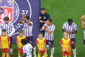 Eine Gruppe junger Jungs steht auf einem grünen Fußballfeld, klatscht in die Hände, mit einem Banner und Logos im Hintergrund.