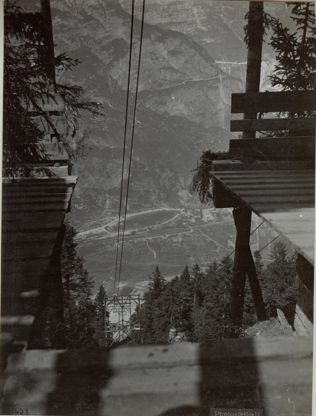 Zwei Seilbahnen mit Text beschriftet fahren einen Berg hinauf, mit Bäumen oben sichtbar.