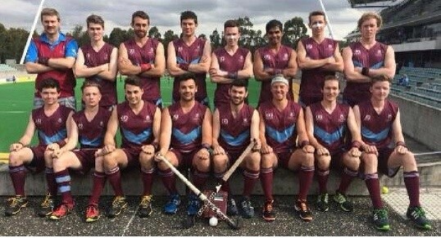 Eine Gruppe von Männern, die auf einem Feld mit Hockeystöcken feiern, mit einem Stadion und Zuschauern im Hintergrund.
