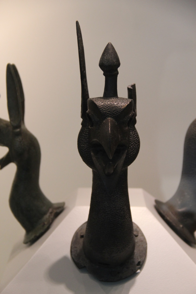 Drei Bronzeplastiken auf einer wei├čen Fl├Ąche in einem Museum ausgestellt, mit einer Wand im Hintergrund.