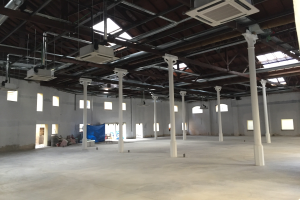 Großer Industriehallenraum mit zahlreichen Fenstern, tragenden Säulen, Deckenbeleuchtung, Klimageräten und offenem Grundriss zur Miete verfügbar.