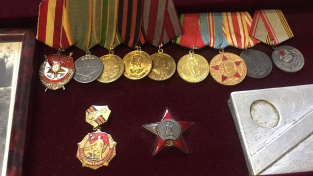 Eine hölzerne Box mit verschiedenen Medaillen, darunter ein roter Stern als Symbol der Sowjetunion, ordentlich angeordnet mit einem Objekt auf der rechten Seite.
