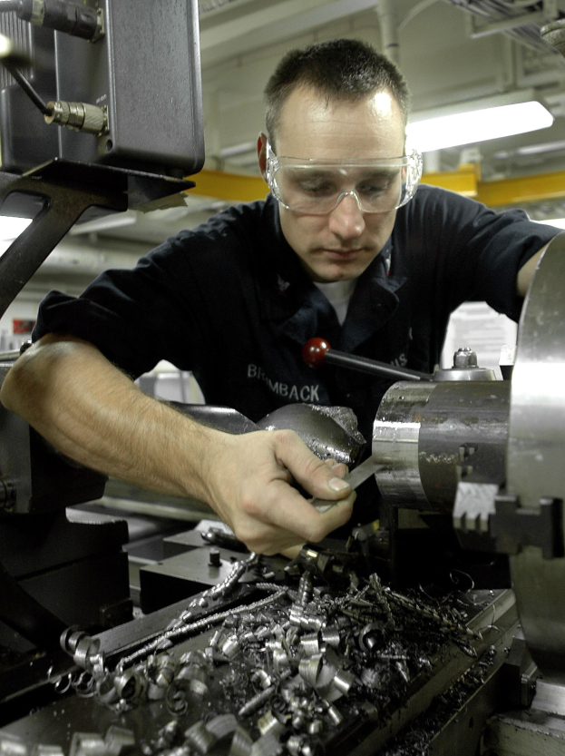 Ein Dreher mit Brille bedient eine Maschine in einer gut beleuchteten Fabrikumgebung.