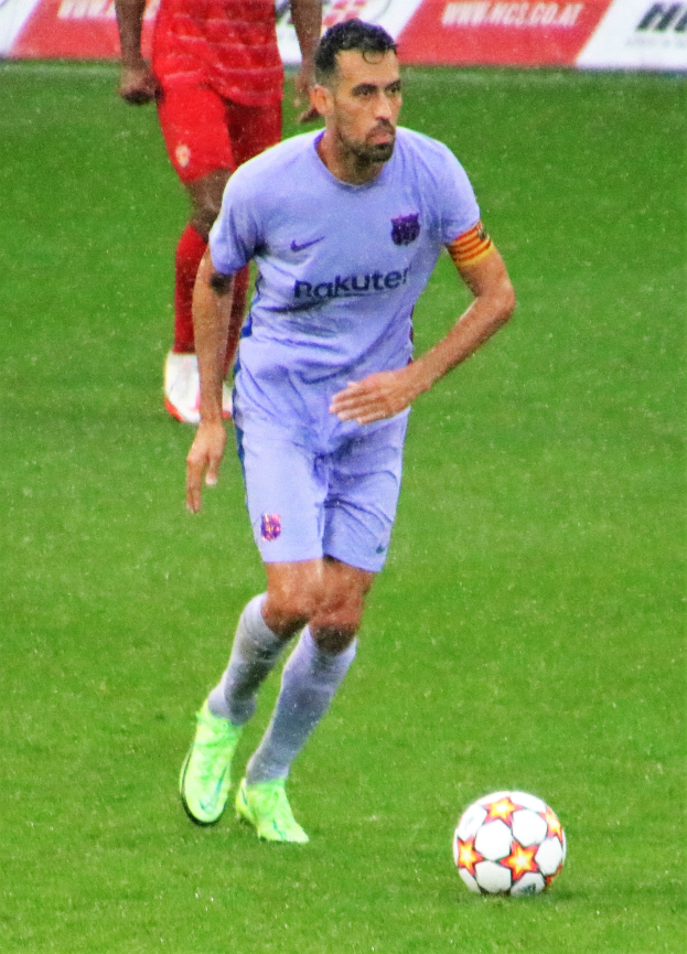 Ein Fussballspieler in einem Sportoutfit und -schuhen ist im Einsatz auf dem Feld, mit einer Texttafel im Hintergrund.