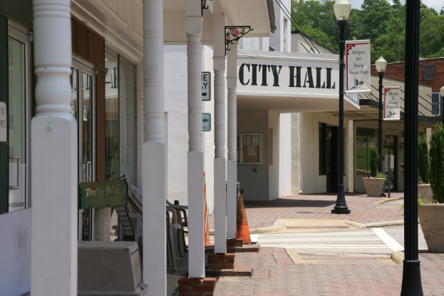 Stadthaus mit umliegenden Gebäuden, Straßeninfrastruktur, Kraftfahrzeugen, Verkehrskegeln, Stühlen, Zimmerpflanzen, Bäumen und einer bewölkten Himmel.