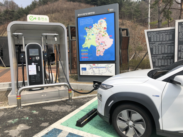 Elektrisches Auto an einer Ladesäule umgeben von Bäumen in Seoul, Südkorea, mit dem Himmel im Hintergrund.
